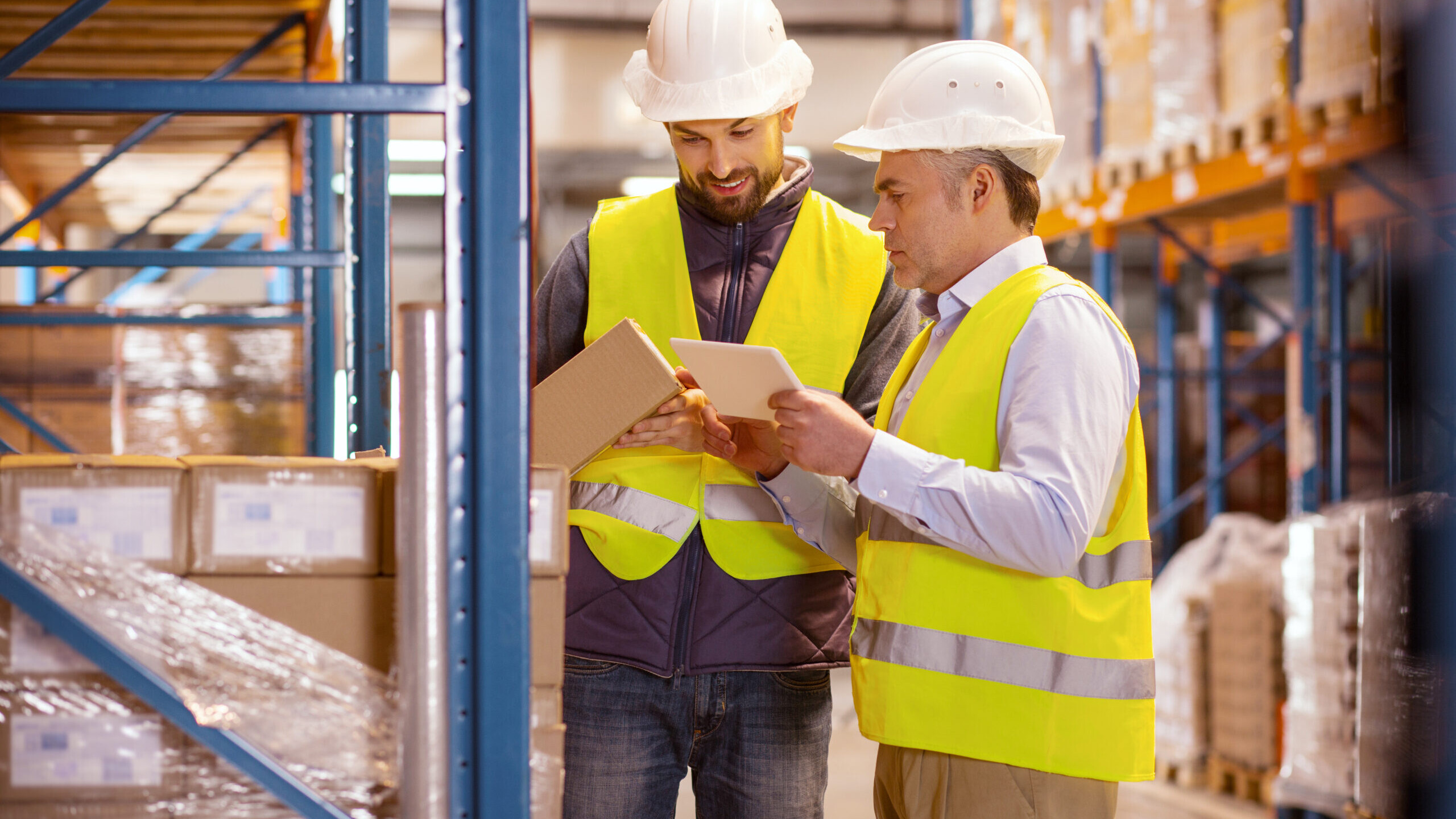 Large scale trade. Delighted nice man holing a box while standing with his colleague in the warehouse to show how important inventory control is.
